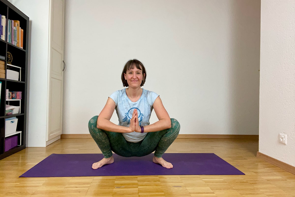 Katharina Balande in der Yin Yoga Stellung "Hocke": Beine gegrätscht, Füsse zeigen nach aussen, Oberschenkel berühren Waden, Hände vor dem Herz.