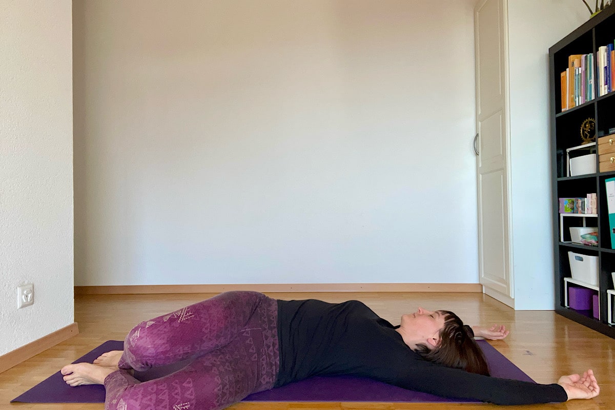 Katharina Balande in der Yin Yoga Stellung Korkenzieher. Rückenlage, Beine gebeugt, Knie aufeinander, fallen zu einer Seite. Arme über den Kopf.