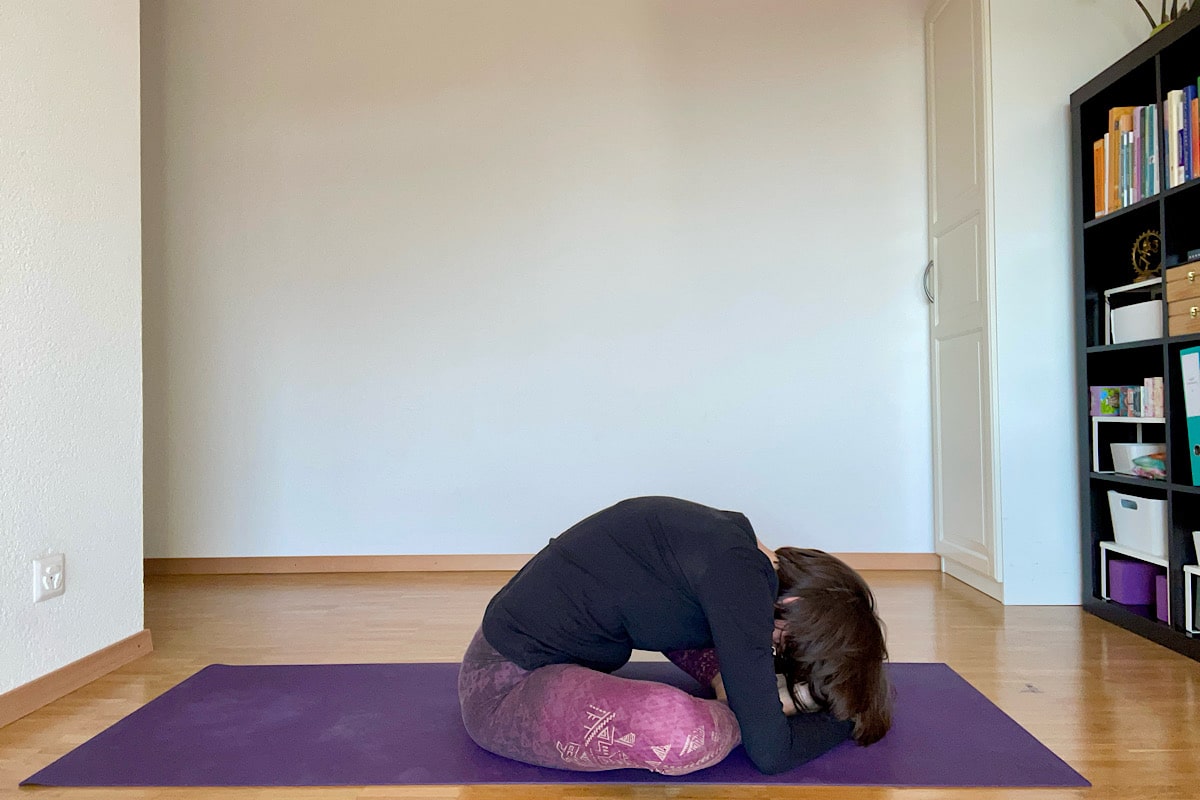 Katharina Balande in der Yin Yoga Stellung "Schmetterling". Sitzend, Beine angewinkelt, Fusssohlen berühren einander, Knie fallen auseinander, Oberkörper nach vorne gebeugt, Kopf hängen.