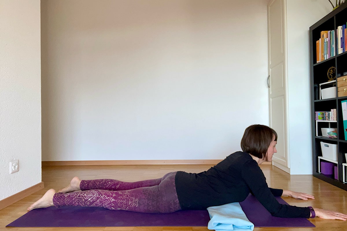 Katharina Balande in der Yin Yoga Stellung "Sphinx". Bauchlage, Oberkörper und Kopf gehoben, Unterarme aufgelegt, Handflächen nach unten. Gefaltete Decke unter dem Rippenbogen.
