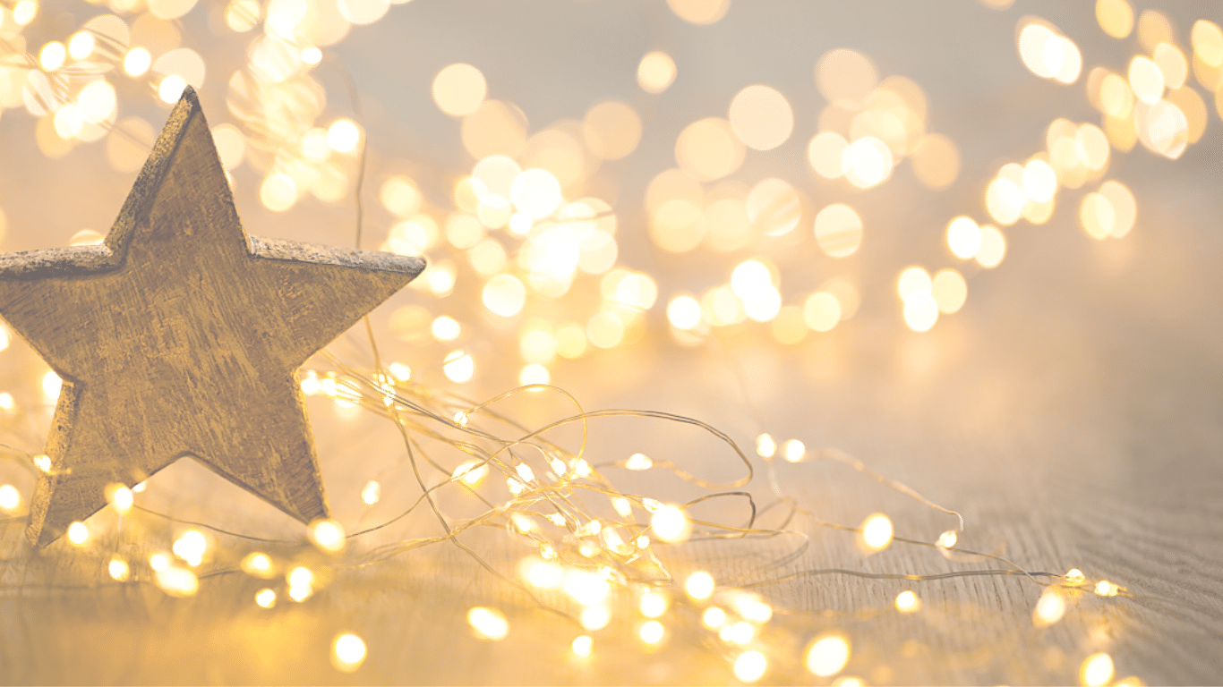 Ein Holzstern, umgeben von sanft leuchtenden Weihnachtslichtern, ruht auf einer Holzoberfläche. Der Hintergrund ist mit warmem, verschwommenem goldenem Bokeh gefüllt, das an die gemütliche Verwandlung des Herbstwandels erinnert und eine festliche Atmosphäre schafft.