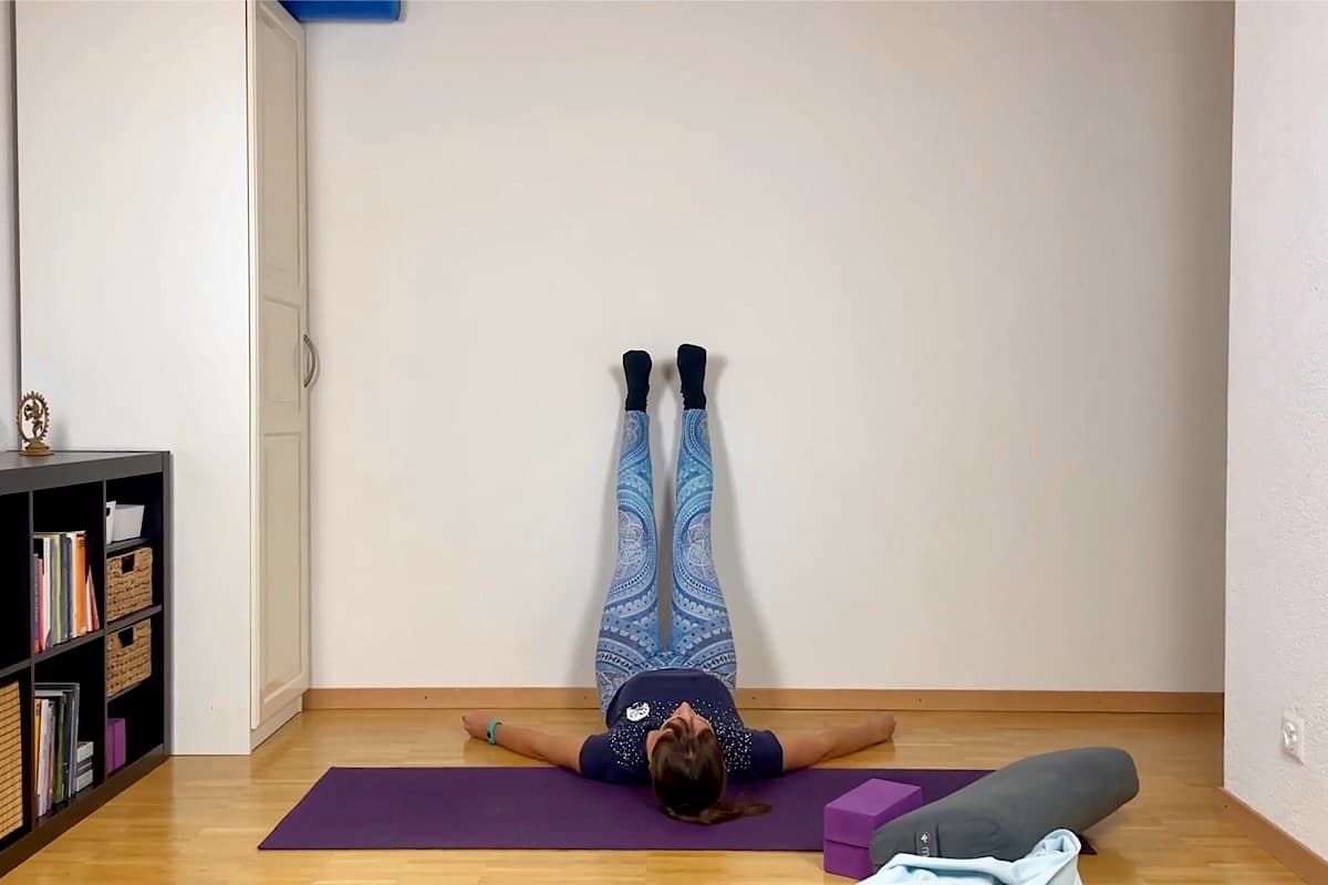 Frau liegt auf dem Rücken und lehnt die Beine gegen die Wand.