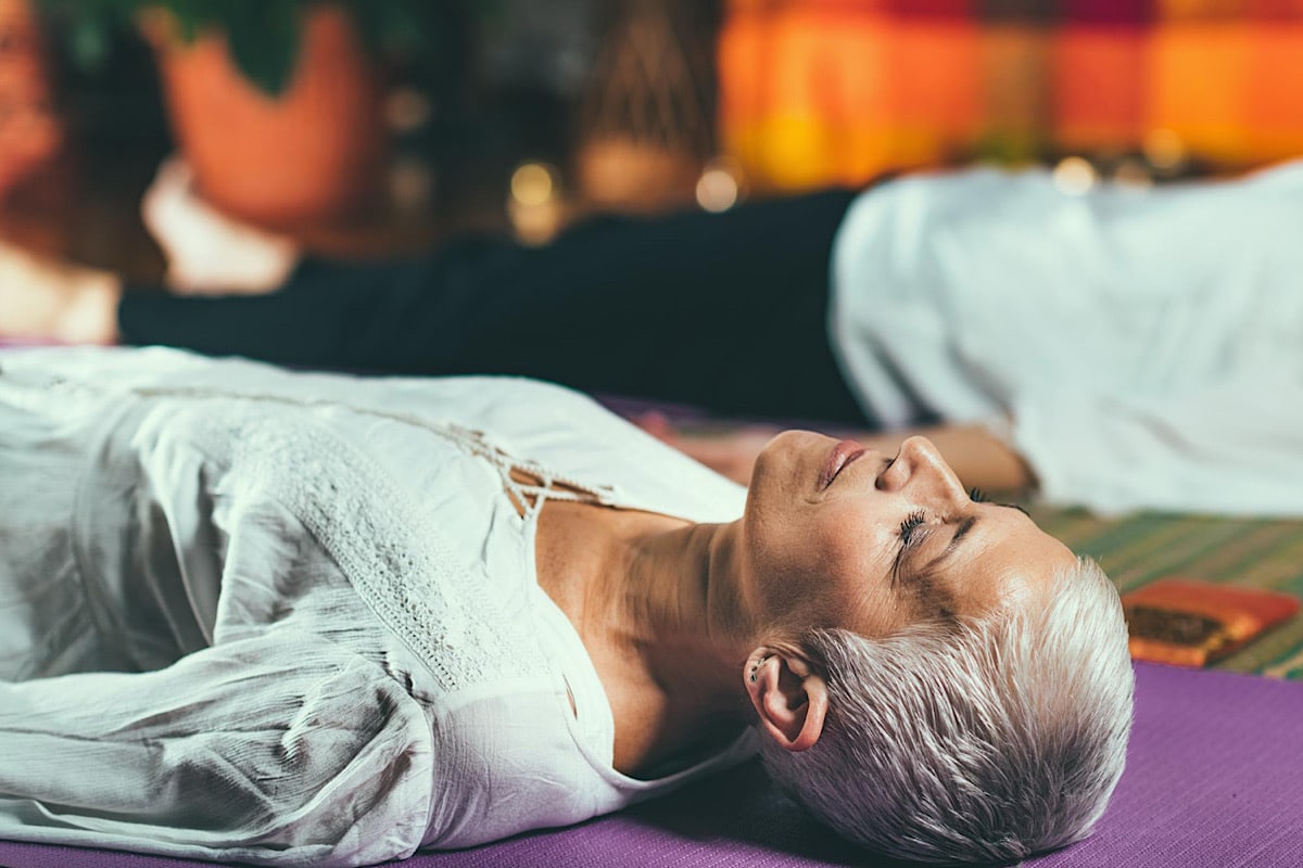 Frau liegt in Savasana auf einer lila Yogamatte mit geschlossenen Augen – die Wirkung von Yoga Nidra zeigt sich in tiefer Ruhe und losgelassenem Körper.
