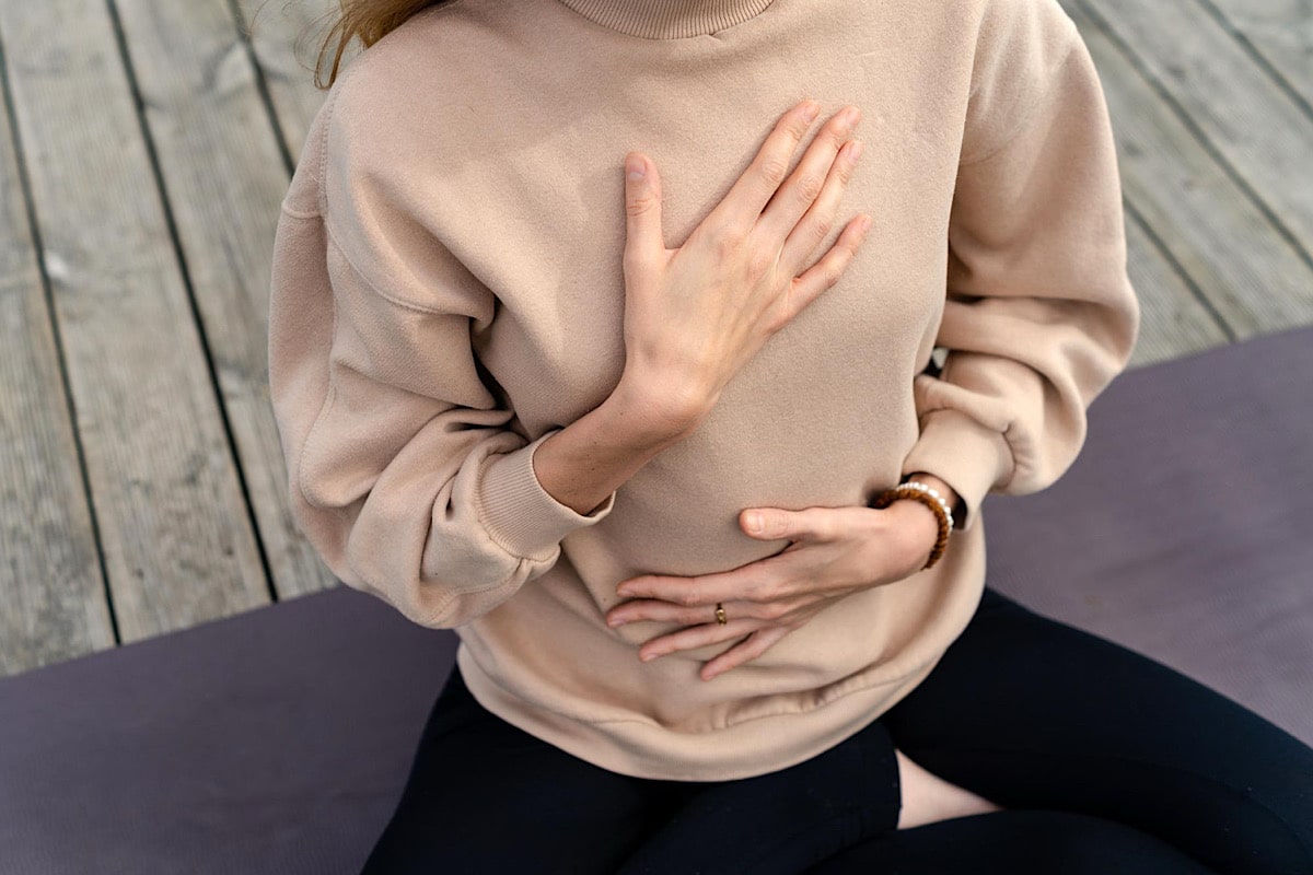 Frau sitzt im Schneidersitz und hält beide Hände auf Brust und Bauch – eine Geste der Körperwahrnehmung, die die physiologische Wirkung von Yoga Nidra spürbar macht.